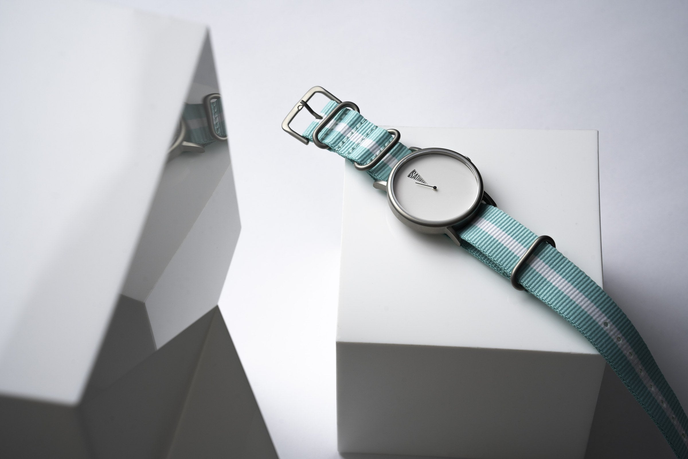 The Point White by Daywatch — studio hero shot on geometric white surface with teal NATO strap