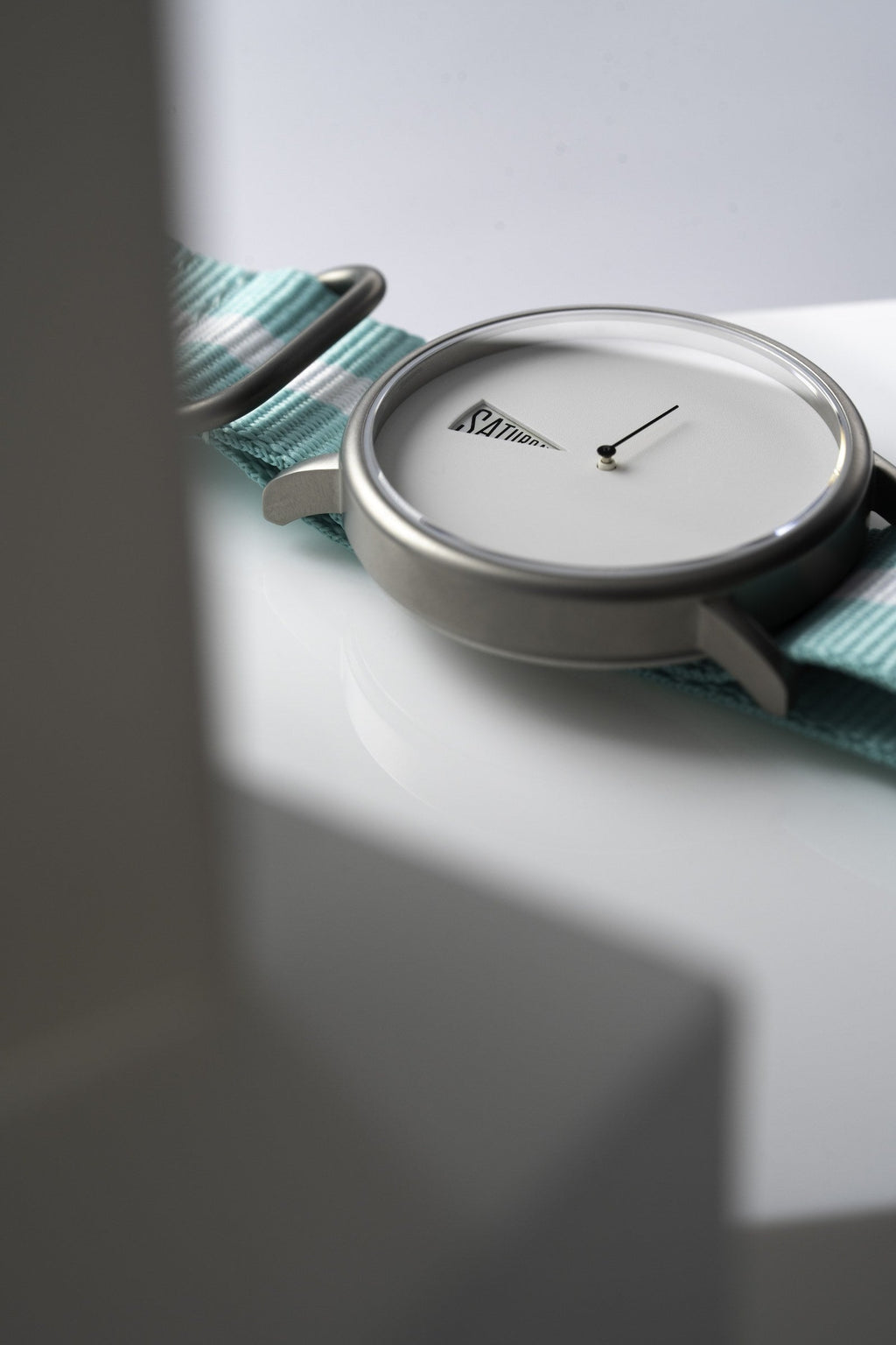 The Point White Daywatch — side profile on white surface showing domed sapphire crystal and teal strap
