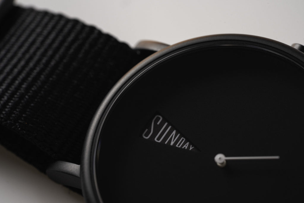 The Point Black Daywatch — close-up dial face showing SUNDAY in white text on black