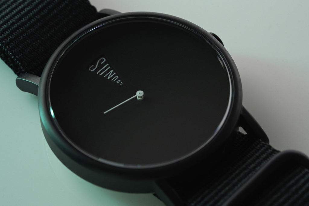 The Point Black Daywatch — side profile on geometric surface with black NATO strap