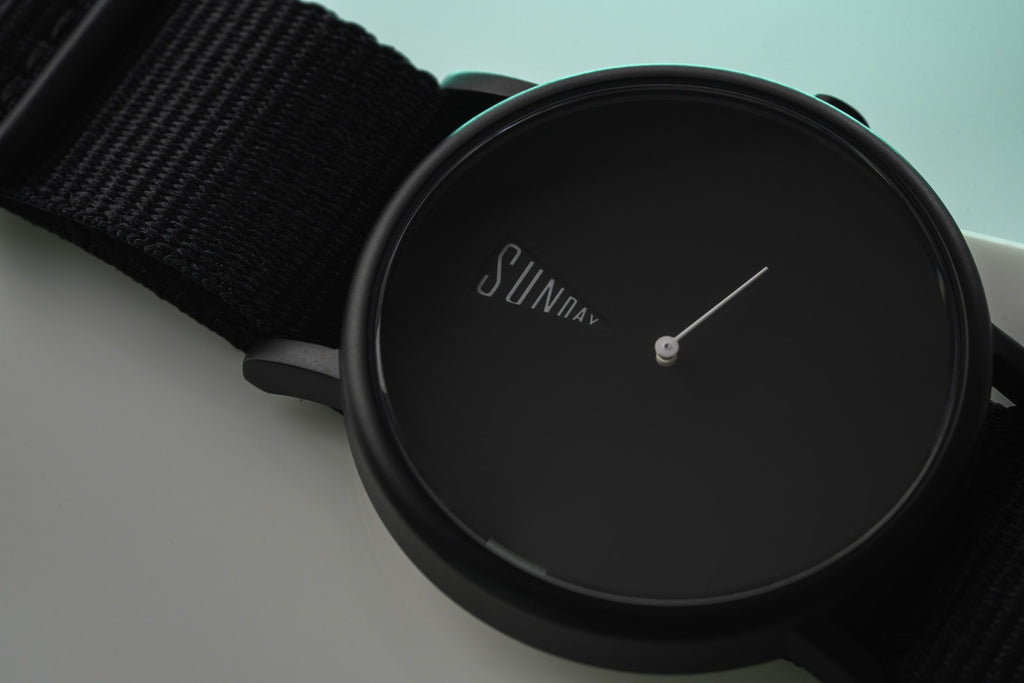 The Point Black Daywatch — flat lay on surface with teal background accent and black NATO strap