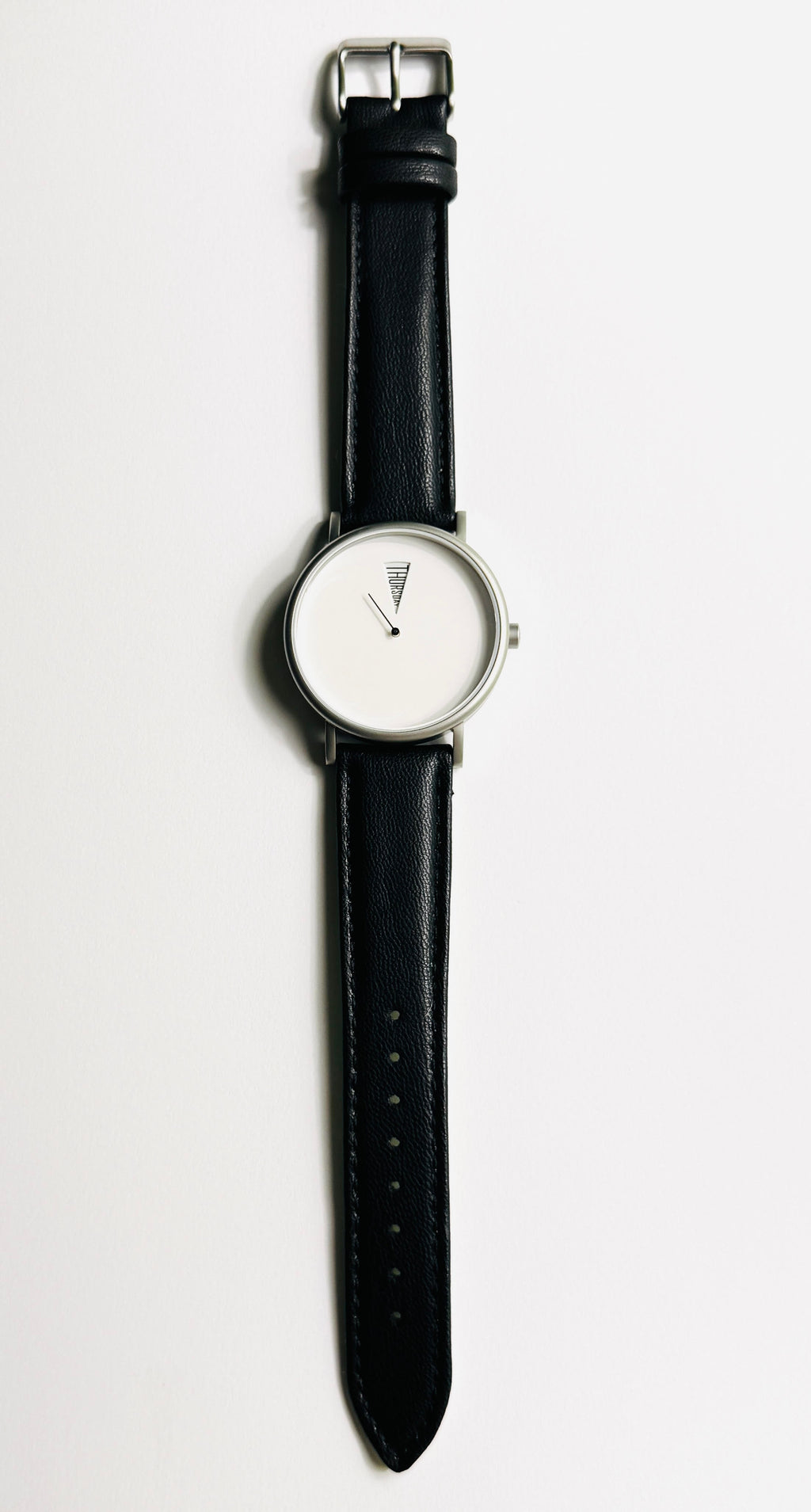 The Point Daywatch flat lay — black pennant watch face detail on neutral background